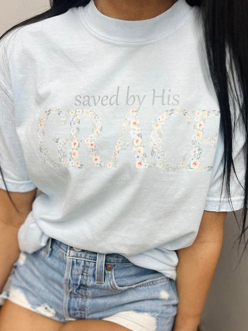 A person wearing a light blue t-shirt with the text 'saved by His grace' and a floral design.