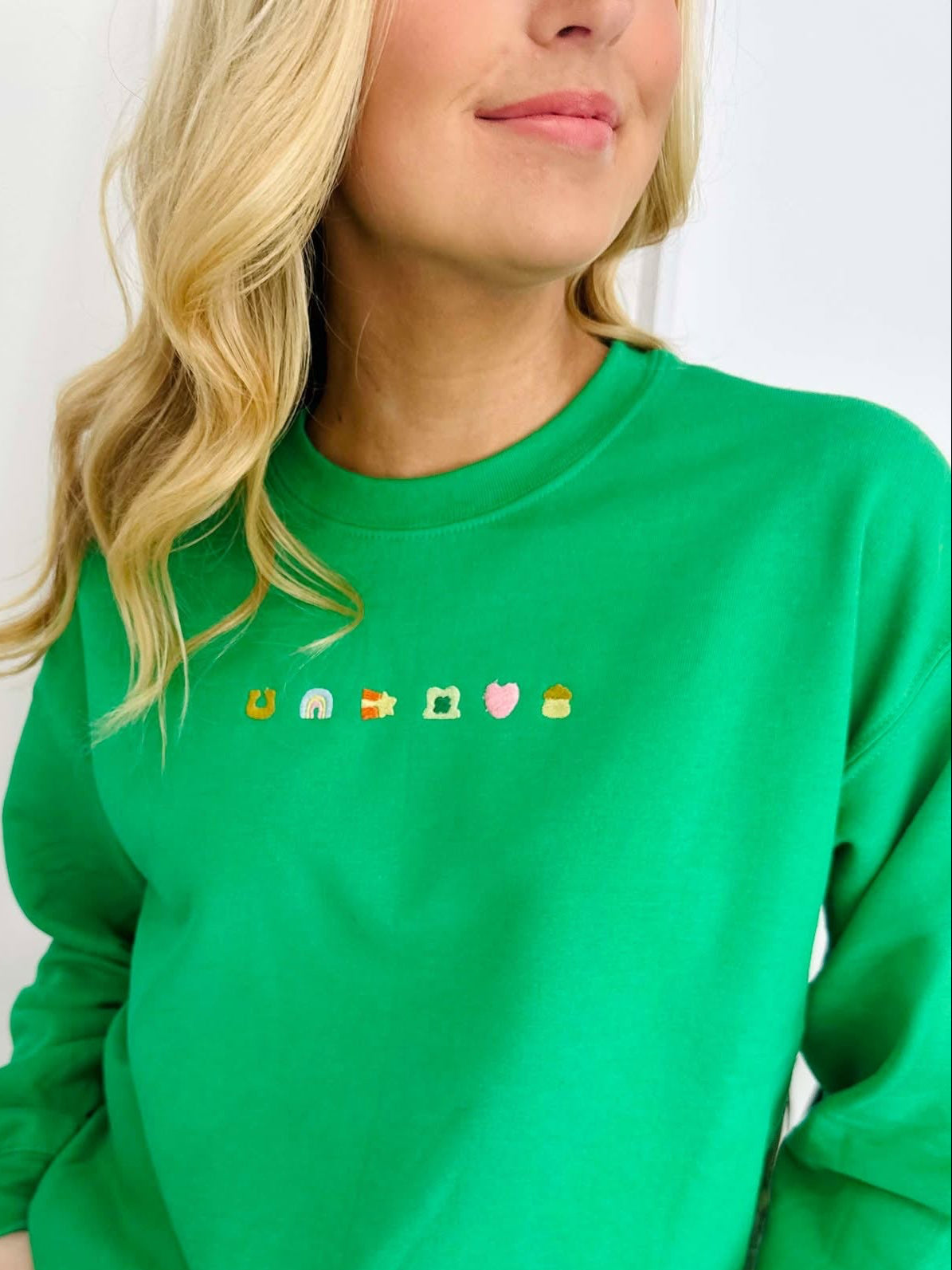 A woman wearing a green embroidered sweatshirt with decorative elements on the front.