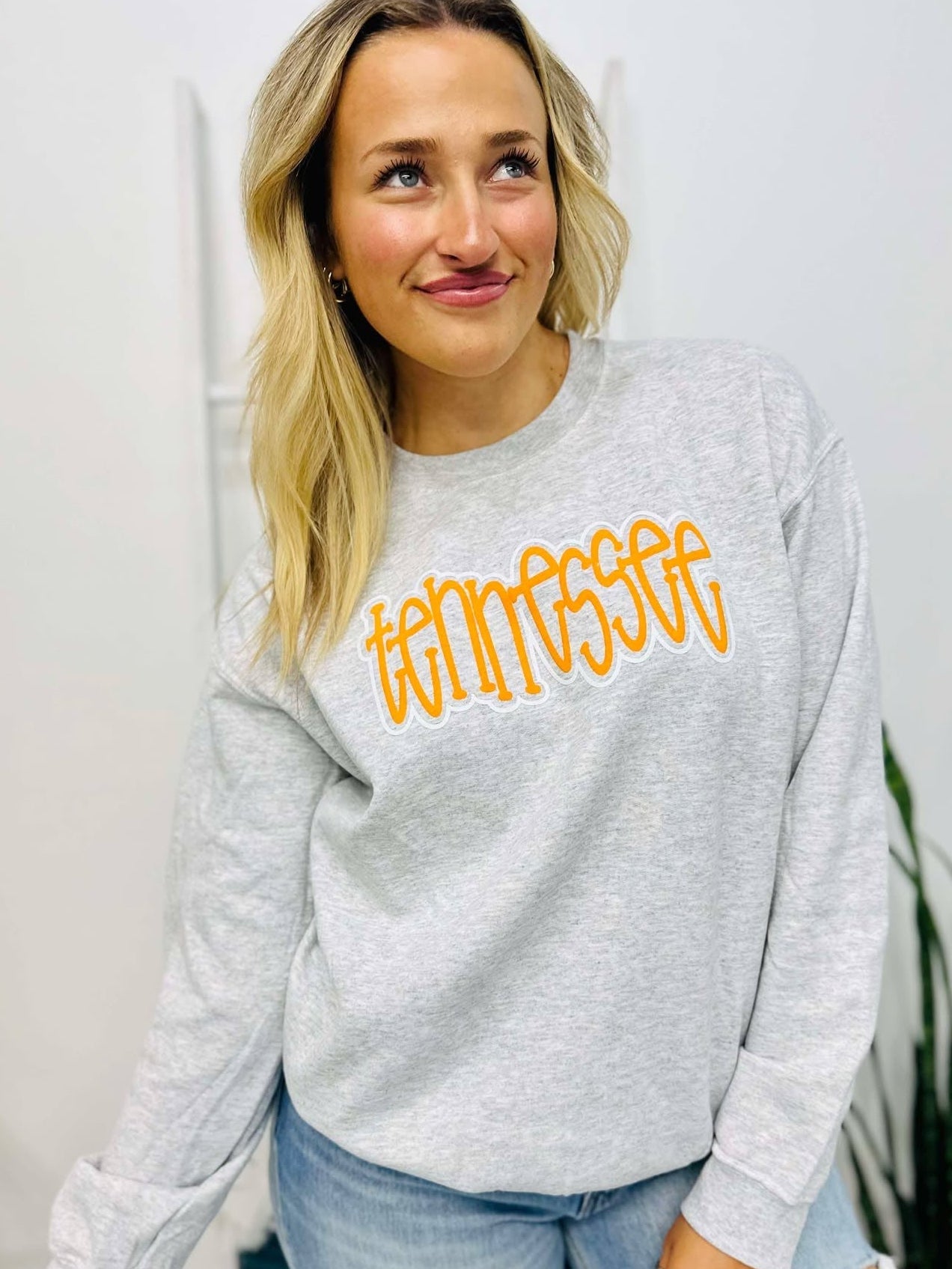 Woman wearing a gray sweatshirt with 'Tennessee' in yellow text, standing indoors.