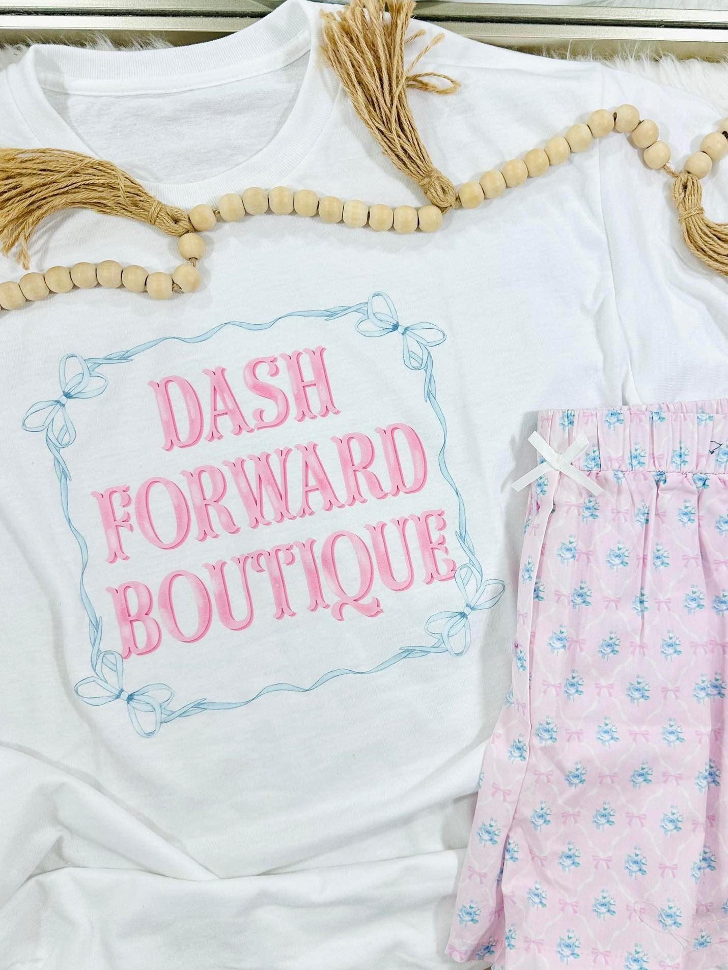 White shirt with 'Dash Forward Boutique' text and pink floral pants on a white background