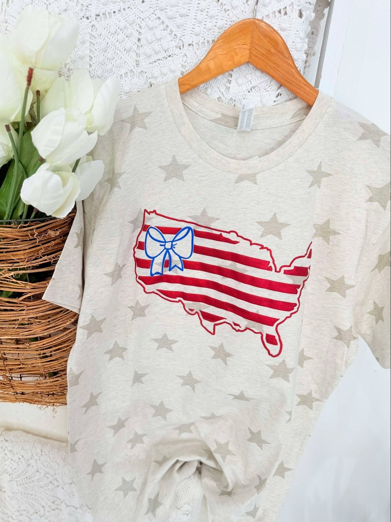 Baby onesie with USA design and bow on stars background next to white tulips in a basket.
