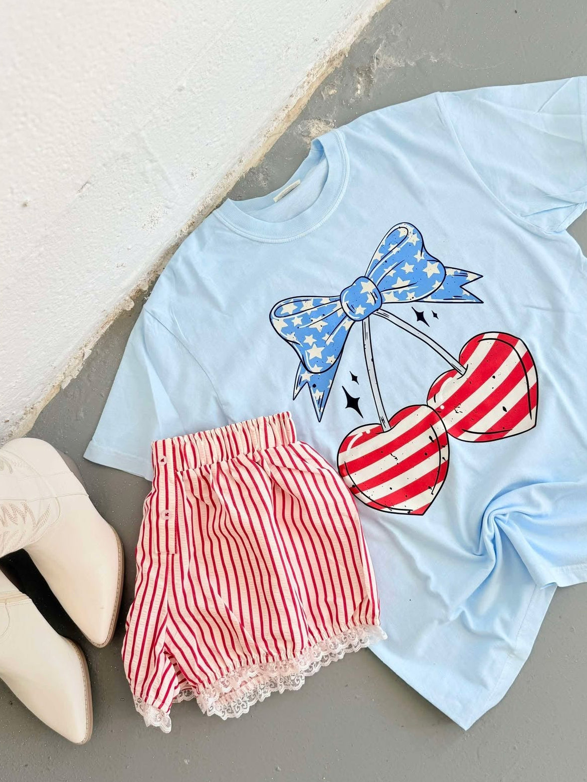Light blue t-shirt with red and white heart cherry design and red shorts on a light gray surface.