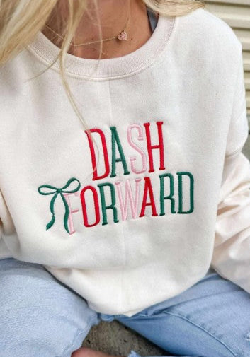 Person wearing a sweet cream sweatshirt with 'DASH FORWARD' text and a green bow embroidery in Christmas colors