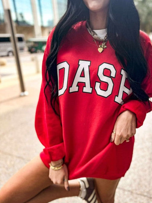 Person wearing a red sweatshirt with 'DASH' varsity custom print on it, standing outdoors.