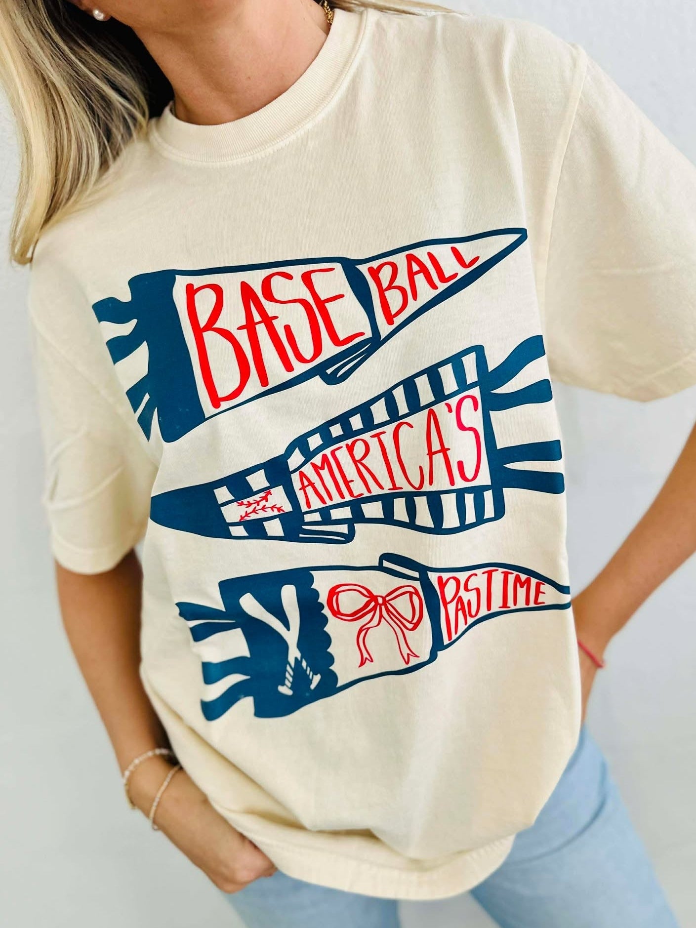 Person wearing a cream t-shirt with 'Baseball America's Pastime' graphic design.