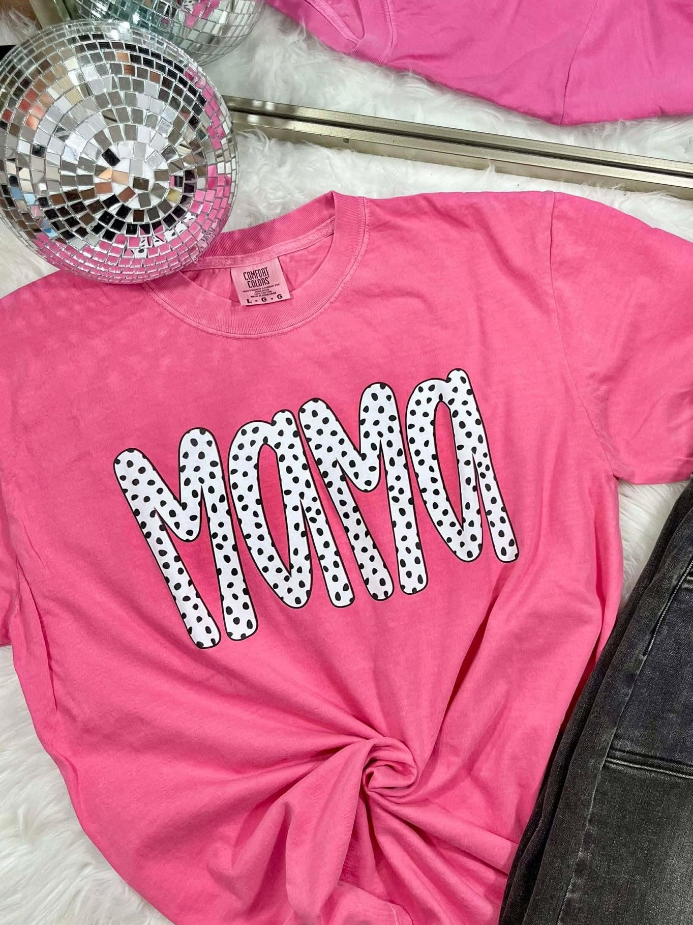 Pink t-shirt with 'MAMA' printed in polka dots, disco ball, and jeans in the background