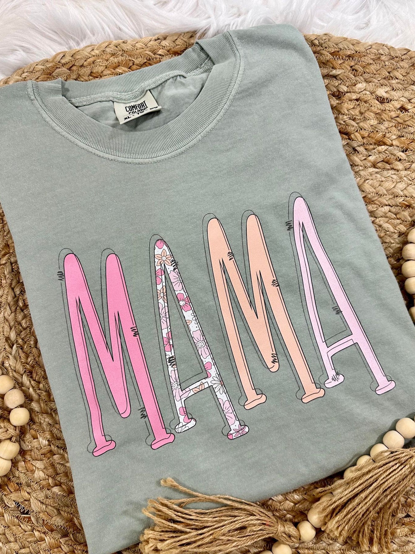 Folded light blue sweatshirt with 'MAMA' in colorful letters on a woven surface.