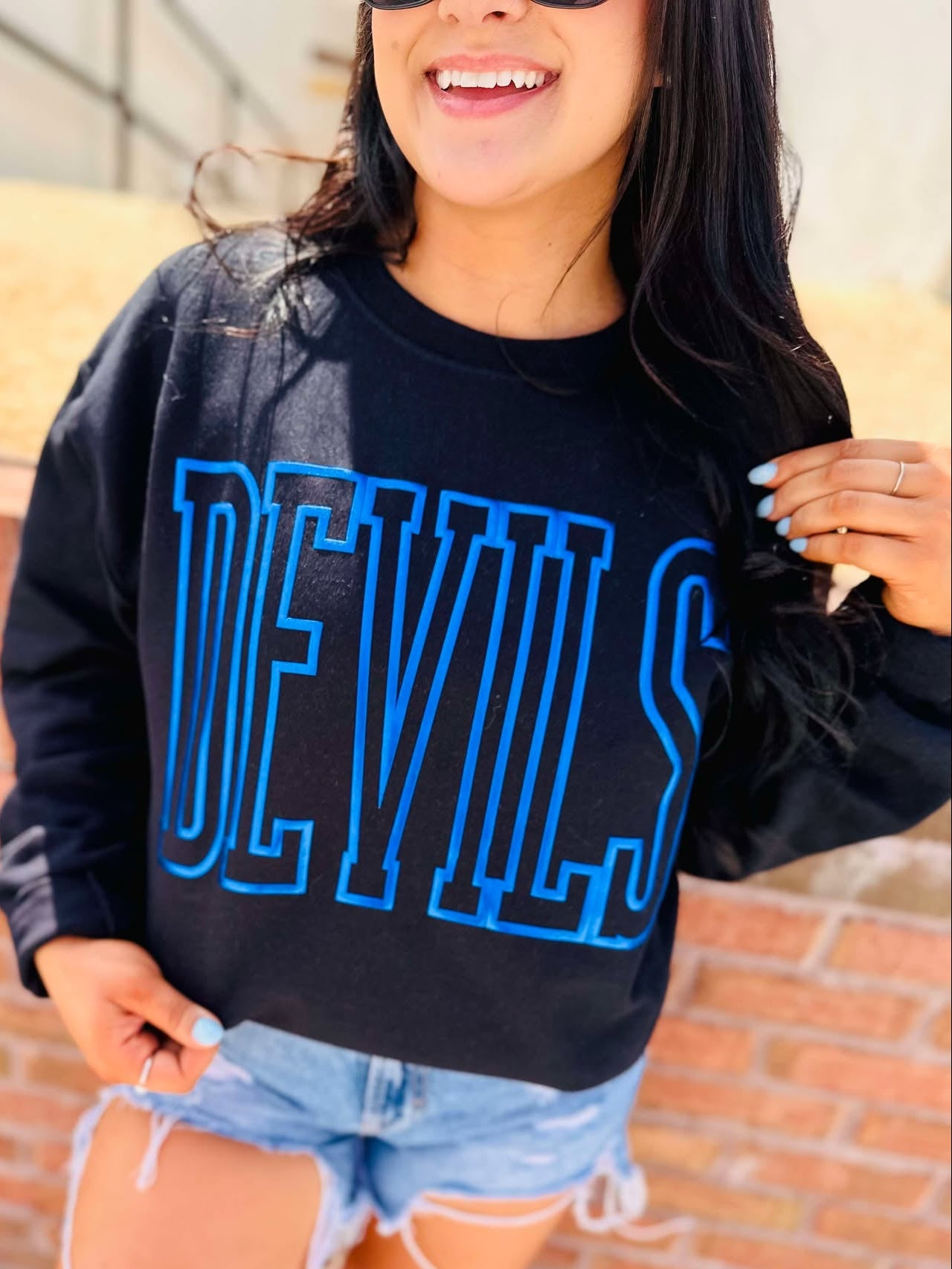 Person wearing a black sweatshirt with 'DEVILS' in blue letters against a brick wall.