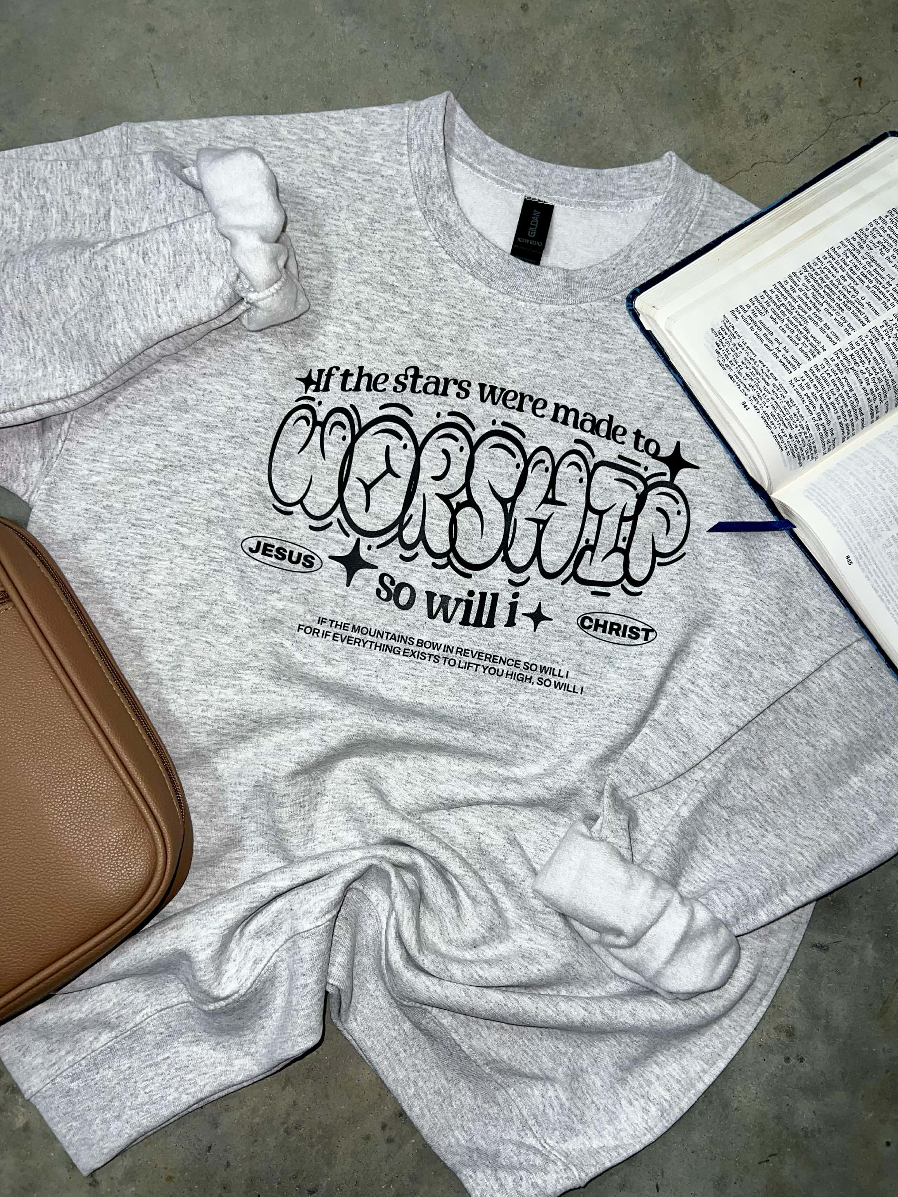 Gray sweatshirt with If the stars were made to worship so will I on a gray surface next to a brown bag and open Bible.