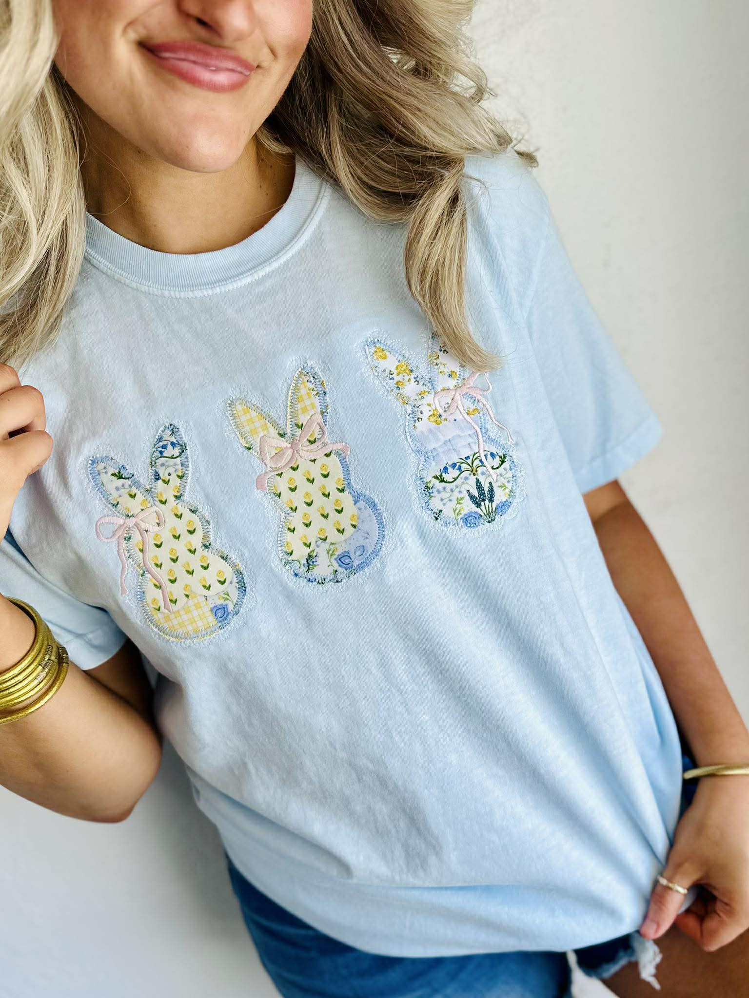 Woman wearing a light blue t-shirt with embroidered designs of Easter bunny bow patchwork and flowers.