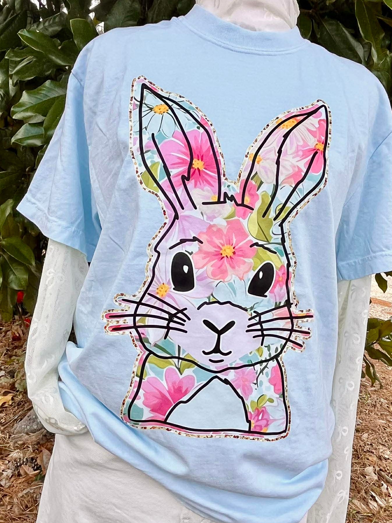 Light blue t-shirt with a floral bunny design on the back, worn by a person outdoors.