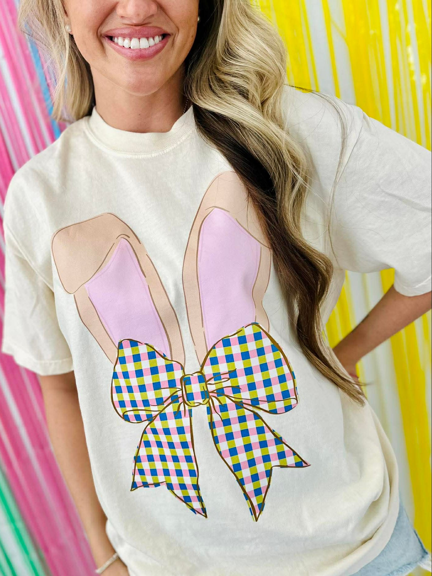 Person wearing a white t-shirt with a colorful Easter Bunny bow design against a multicolored striped background