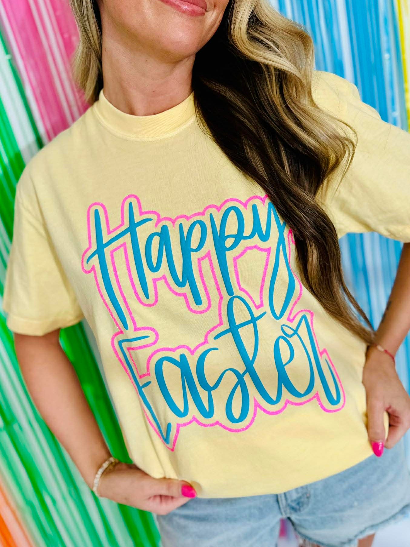 Woman wearing a yellow 'Happy Easter' t-shirt in front of a colorful striped background