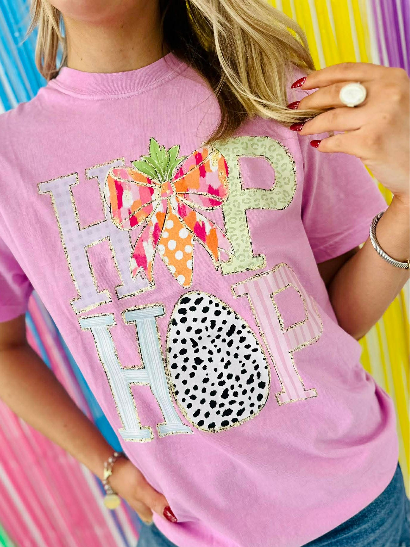 Person wearing a pink t-shirt with decorative HIP HOP letters and patterns against a colorful striped background