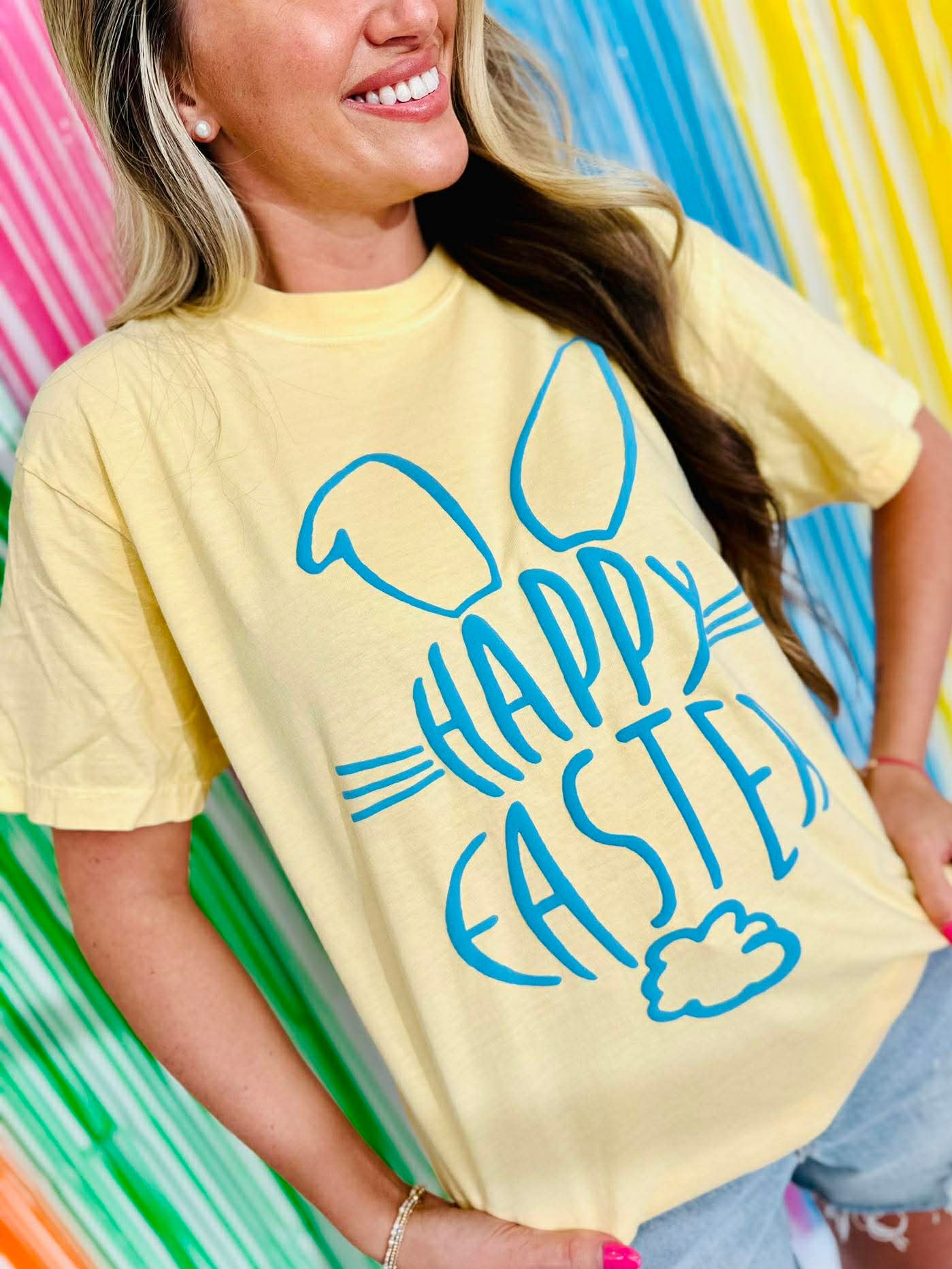 Person wearing a yellow t-shirt with 'Happy Easter' Bunny cotton tail Puff vinyl design against colorful striped background