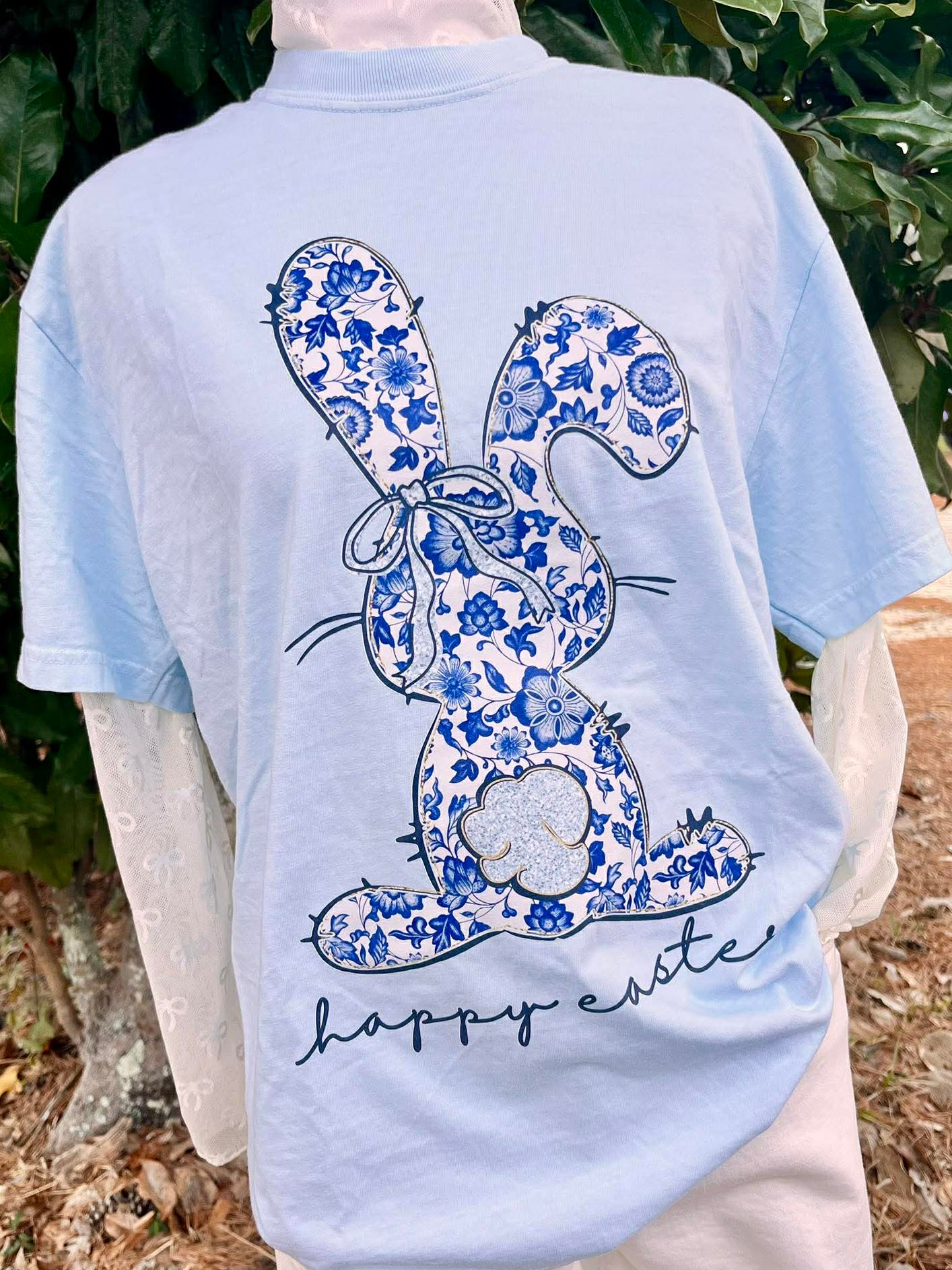 Light blue t-shirt with a blue floral chino bunny design and 'Happy Easter' text, worn outdoors.