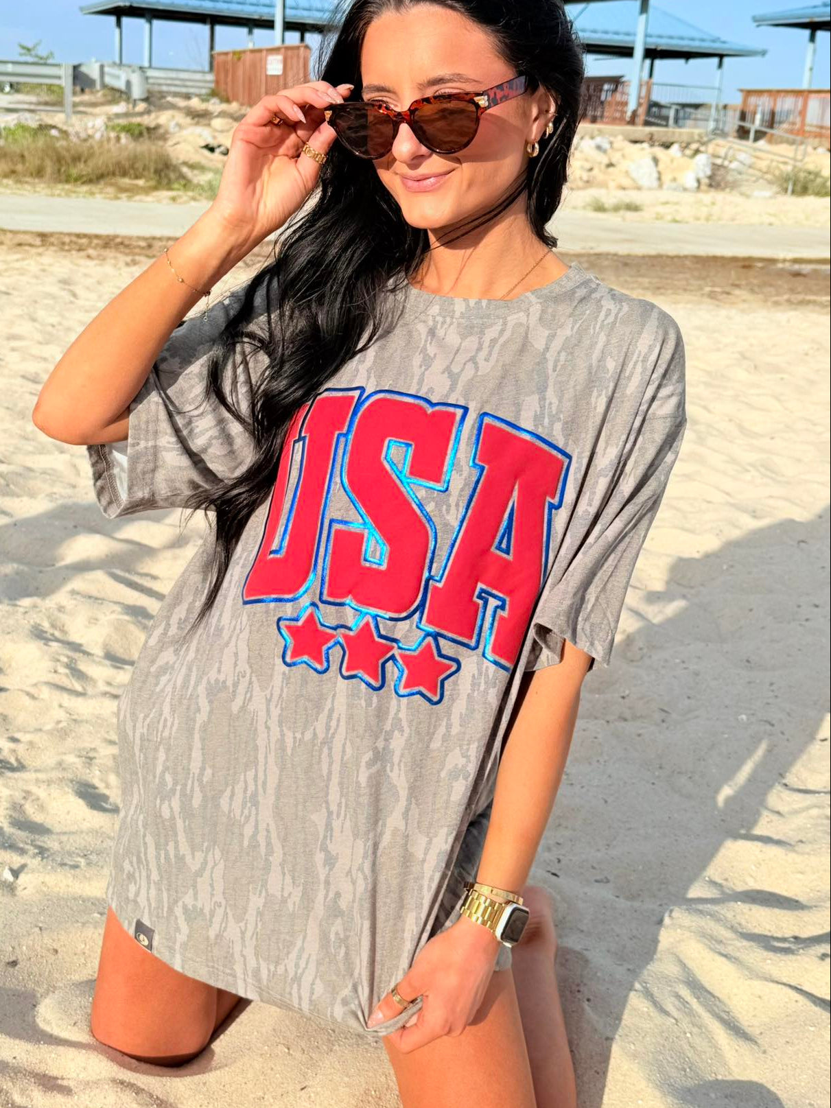 Woman wearing a bottomland 'USA' t-shirt on a sandy beach.