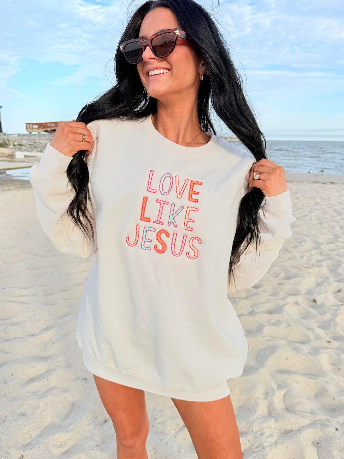 Woman wearing a 'Love Like Jesus' embroidery shirt on a beach