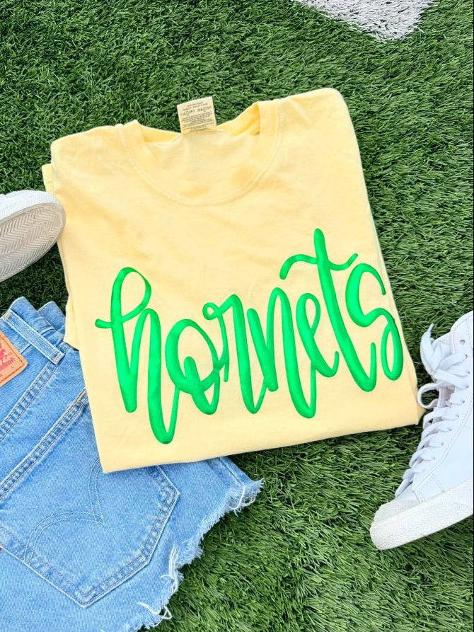 Yellow sweatshirt with 'hornets' text, blue jeans, and white sneakers on grass