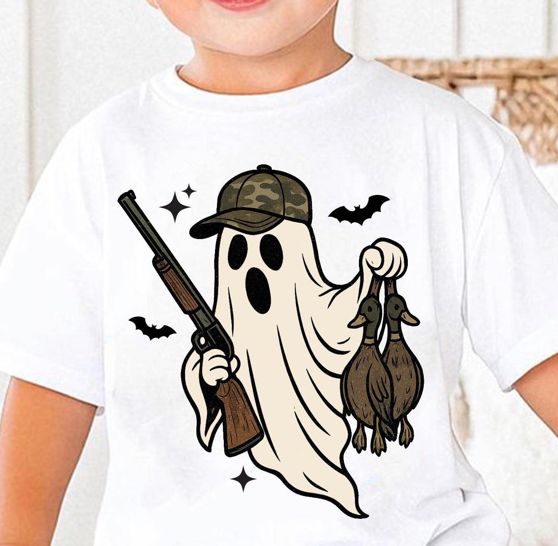 Child wearing a white t-shirt with a camo ghost holding a gun and two ducks design.