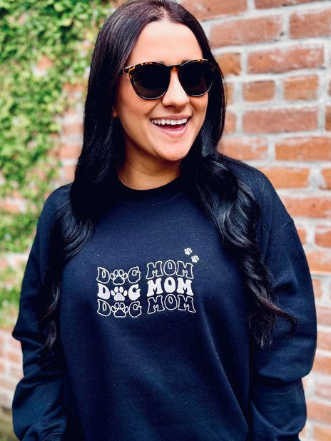 A woman smiling and wearing a black sweatshirt with the text 'Dog Mom' and a small wave symbol embroidered on it.