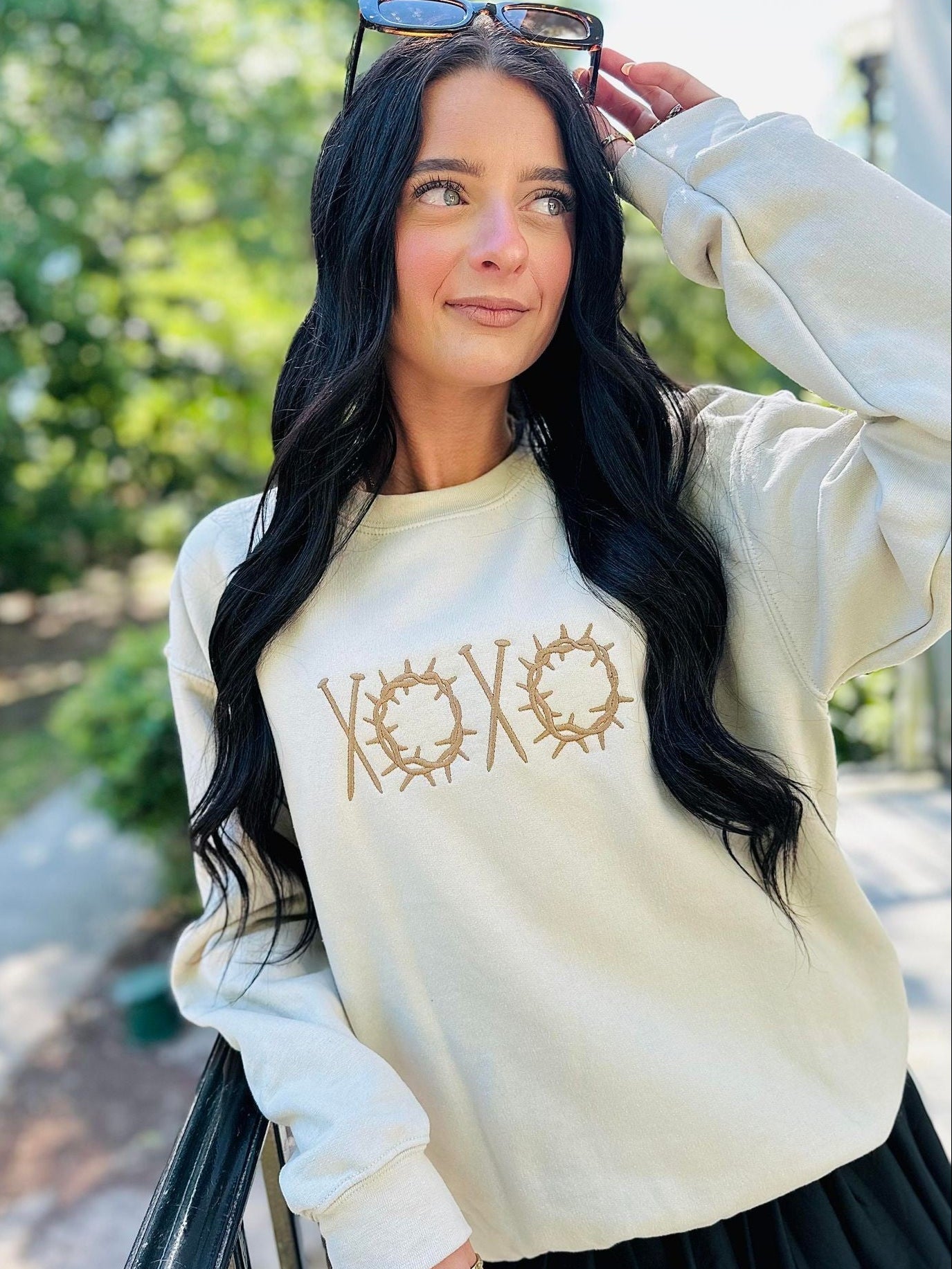 Woman wearing a cream-colored sweatshirt with 'XOXO' design outdoors.