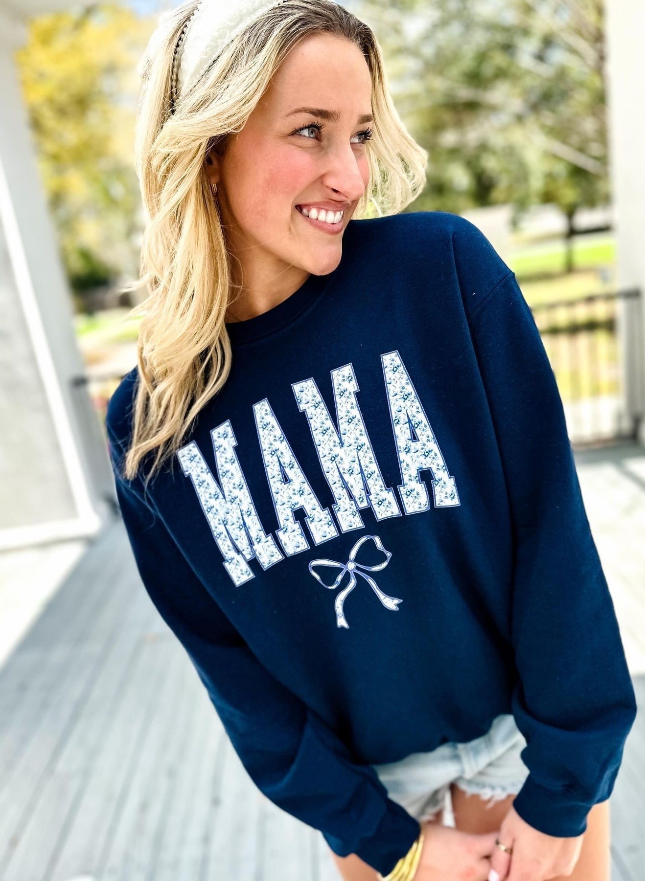 Woman wearing a navy blue sweatshirt with 'MAMA' printed on it, standing outdoors.