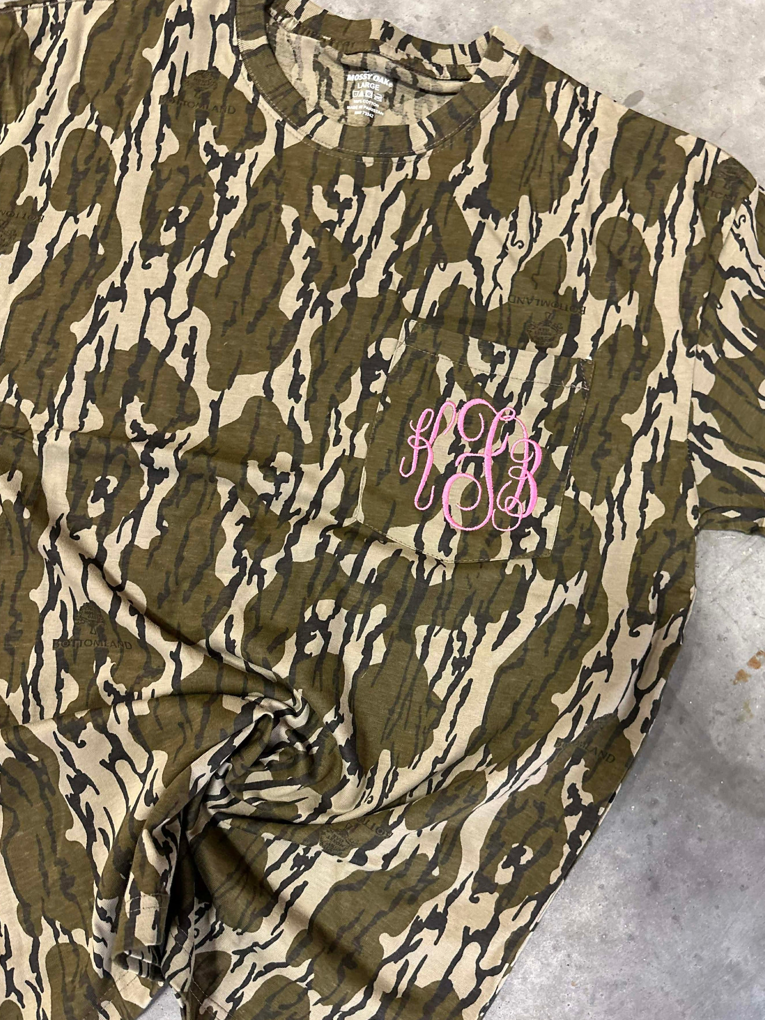 Camouflage-patterned shirt with pink monogram on a textured surface