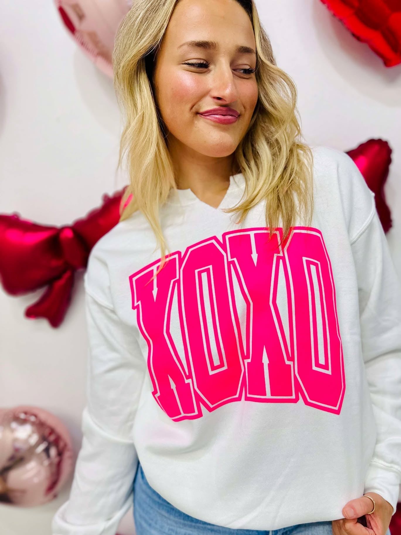 A person wearing a white V-neck sweatshirt with 'XOXO' printed in neon pink vinyl on the front.