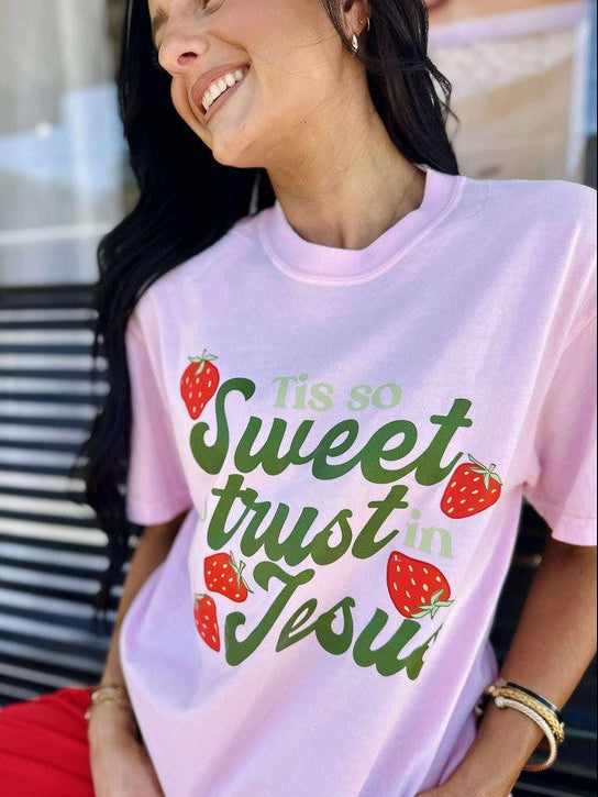 Woman wearing a pink t-shirt with text and strawberry graphics, sitting outdoors.