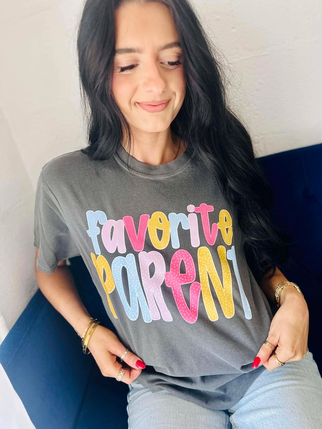 Woman wearing a gray t-shirt with 'Favorite Parent' in polka dot colorful letters, sitting on a blue couch.