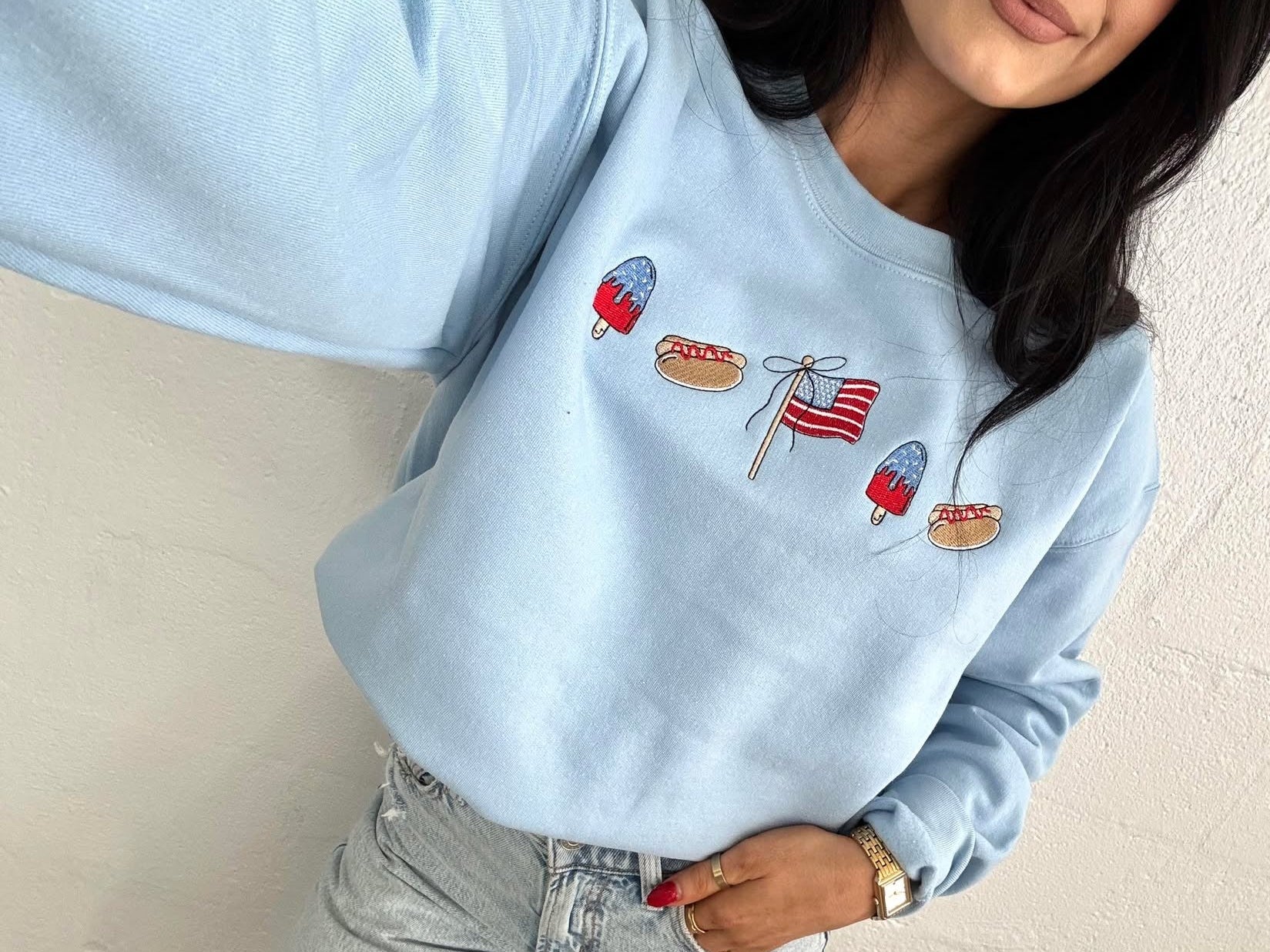 Person wearing a light blue sweatshirt with embroidered designs against a plain background