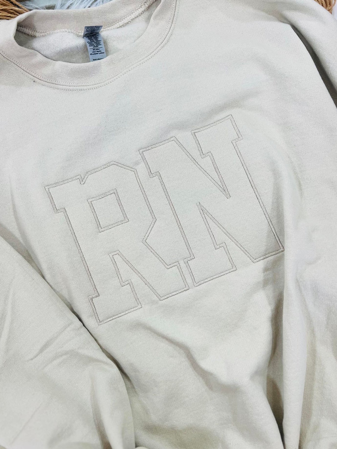 A beige embroidered sweatshirt with the letters 'RN' on the front.