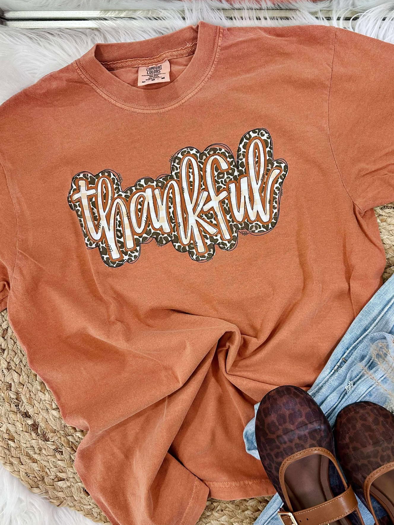 Copper t-shirt with 'thankful' design, leopard print shoes, and denim shorts on a textured surface.