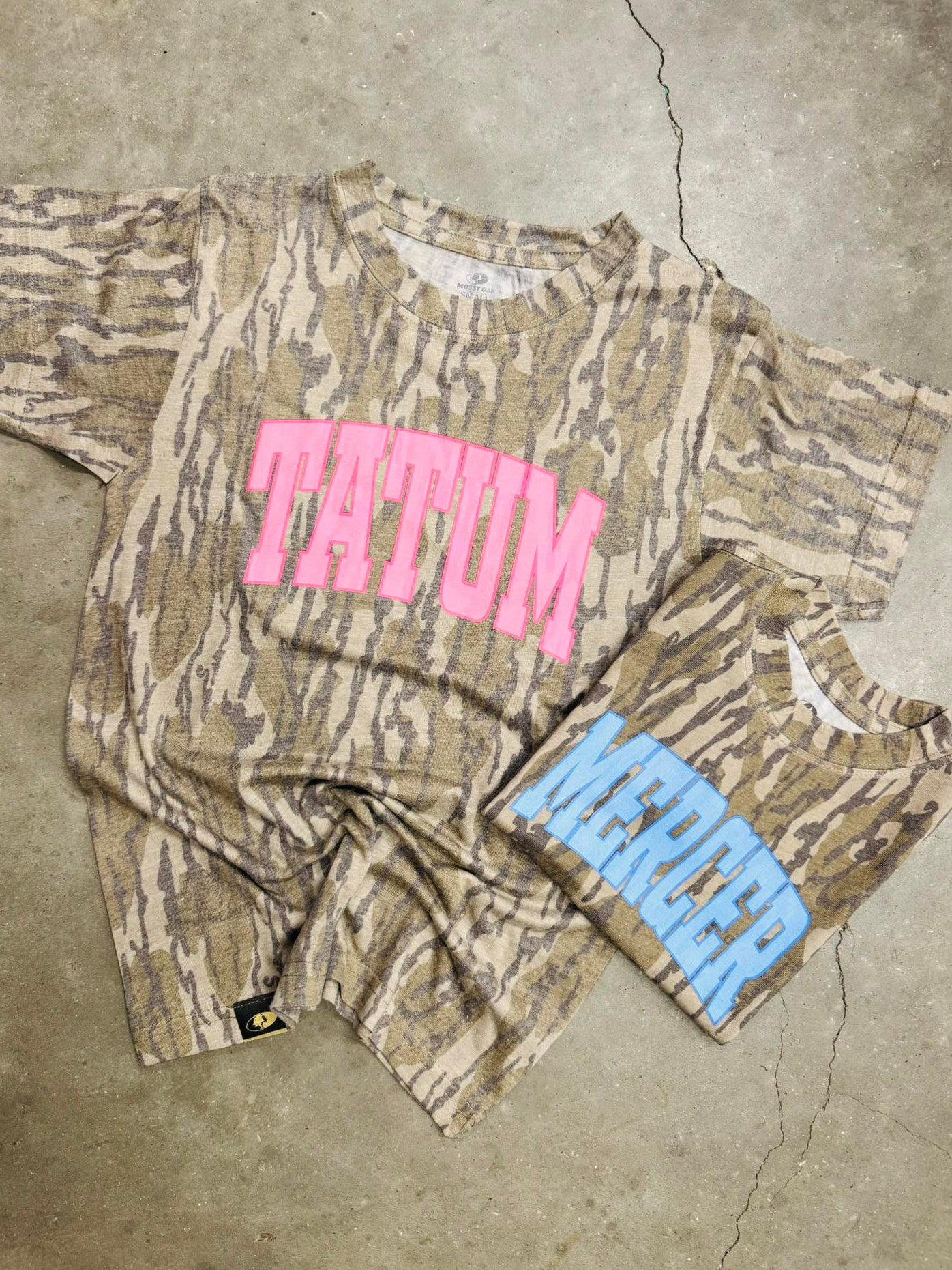 Camouflage t-shirt with pink text and blue shorts on a concrete floor