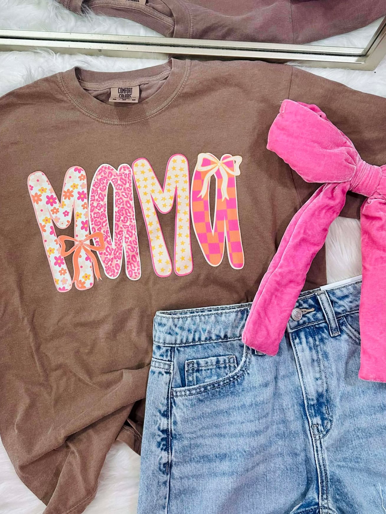 Brown t-shirt with 'MAMA' print, pink shorts, and denim shorts on a white surface.