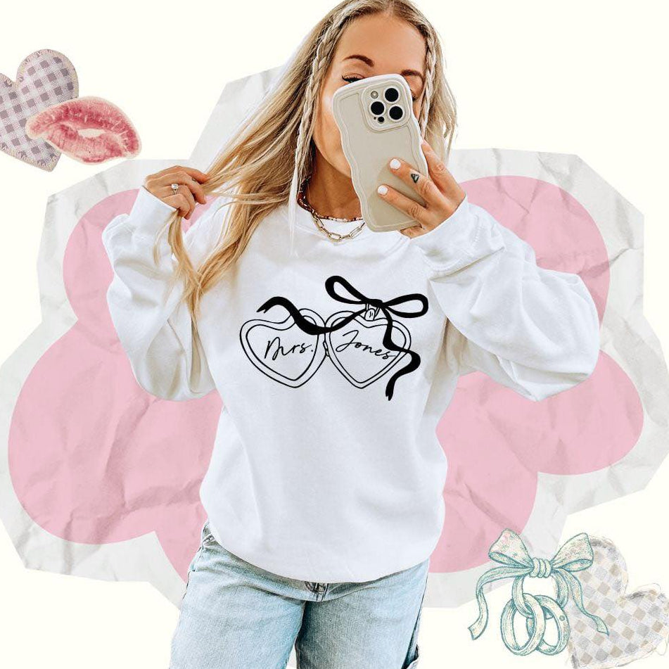Person wearing a white sweatshirt with a Mrs. Jones bride graphic design, standing against a white background with decorative elements.