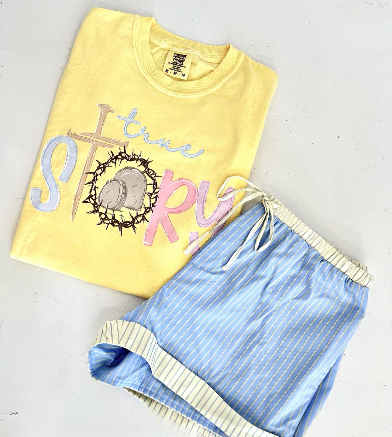 Yellow t-shirt with 'true story' text and blue shorts on a light gray background