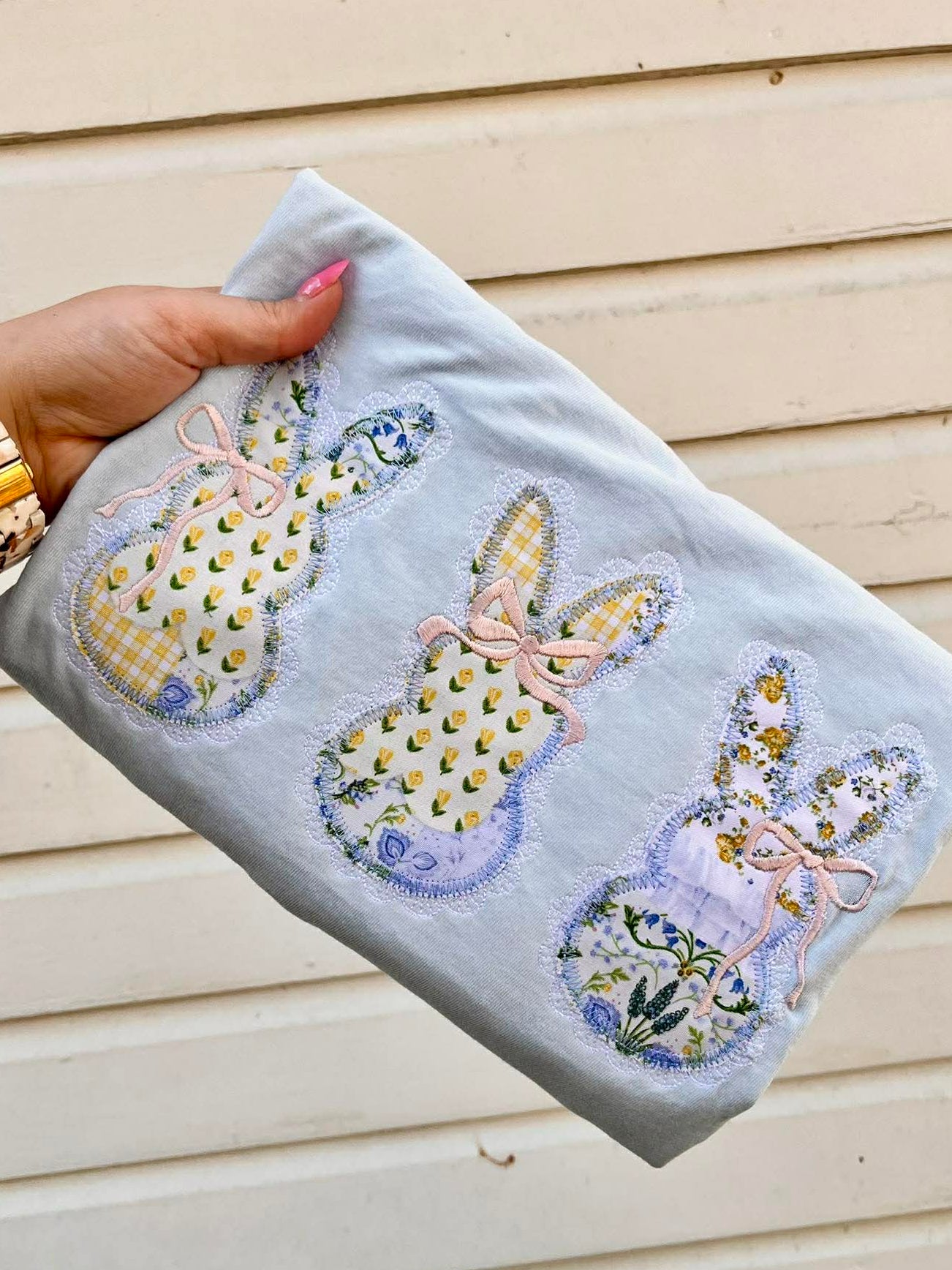 Hand holding a folded embroidered tee with lace bunny designs against a wooden background