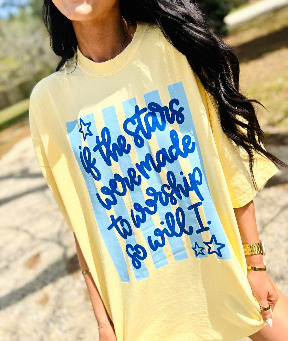 Person wearing a yellow t-shirt with blue text and star graphics outdoors.
