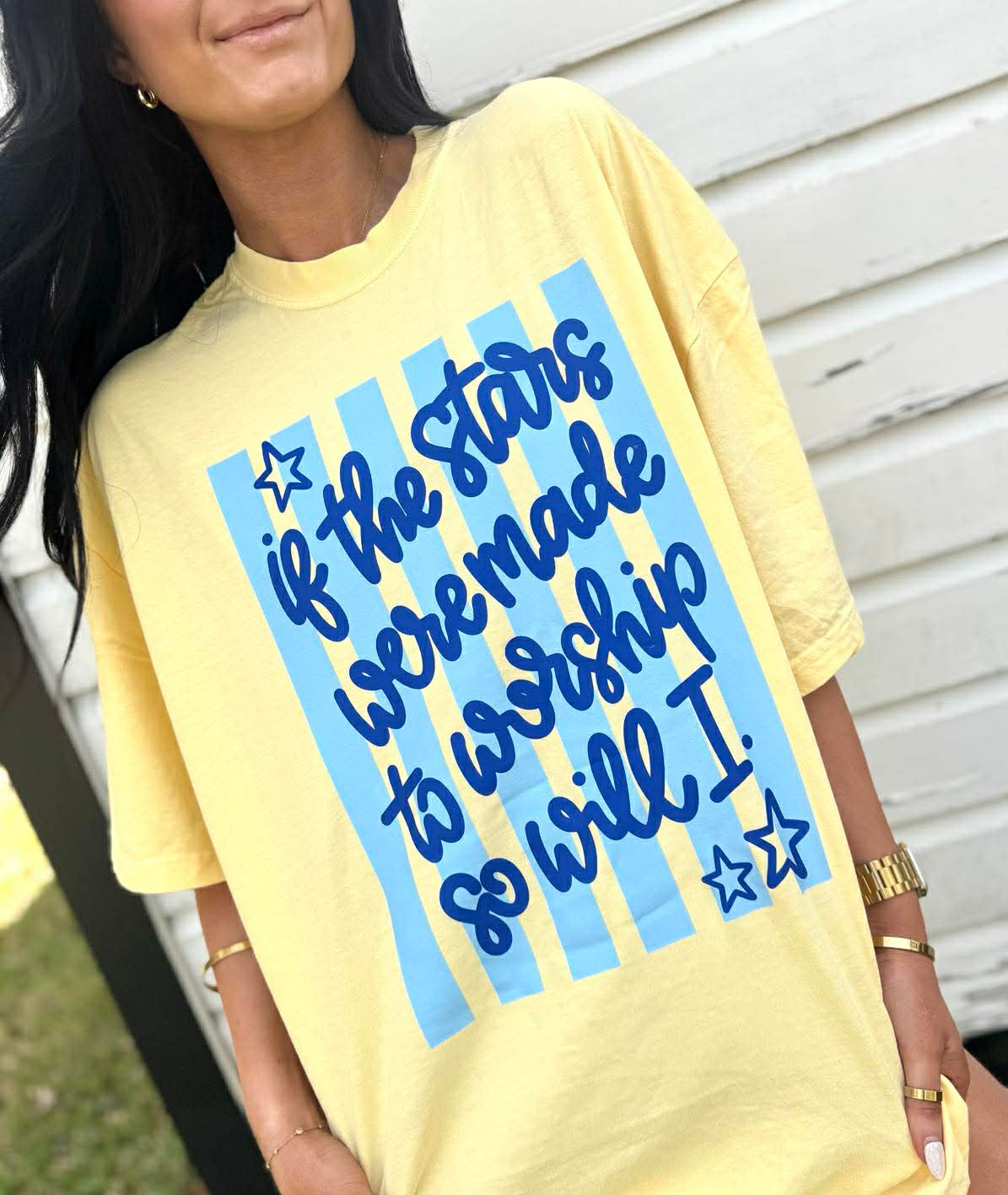 Person wearing a yellow t-shirt with blue text design "If the stars were made to worship so will I"