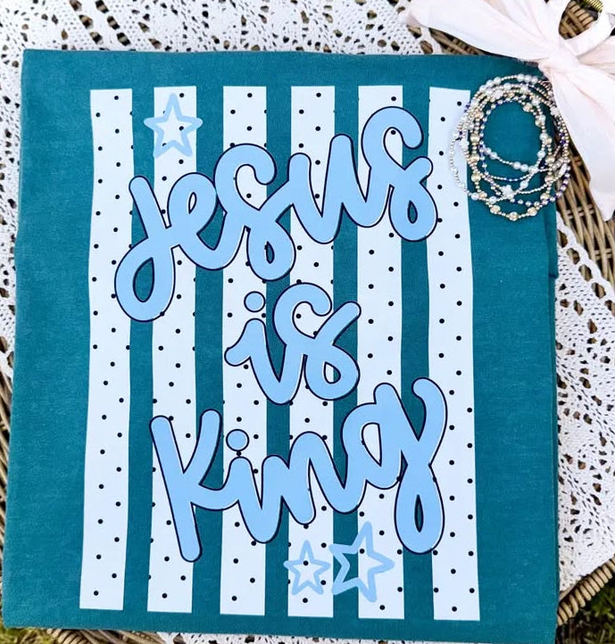 Card with 'Jesus is King' text on a blue and white striped background, placed on a textured surface.