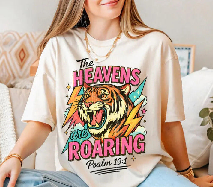 Person wearing a t-shirt with a graphic design of a tiger and text "Heavens are roaring", sitting on a couch.