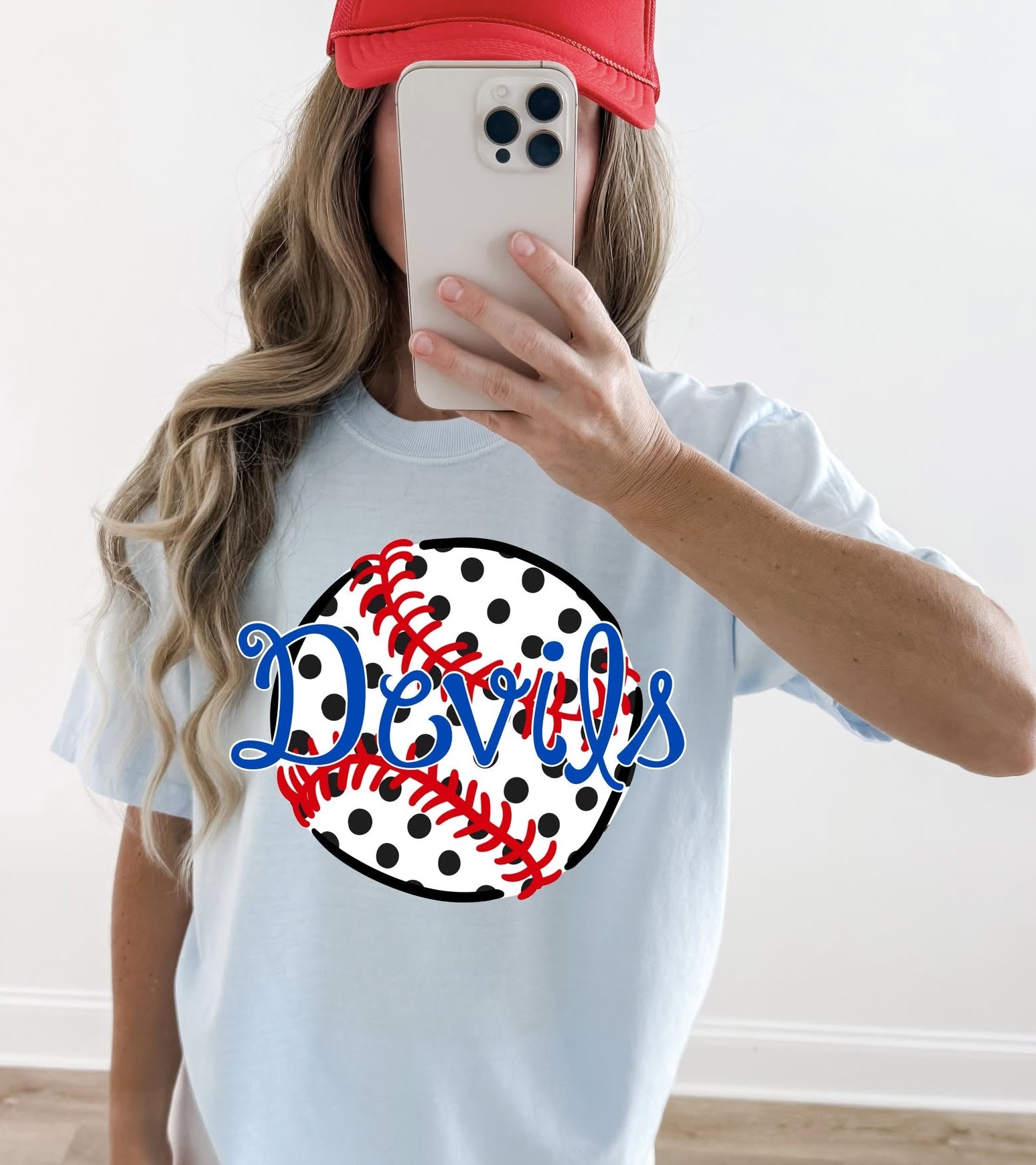 Person wearing a white t-shirt with 'Devils' and a baseball design, taking a mirror selfie.