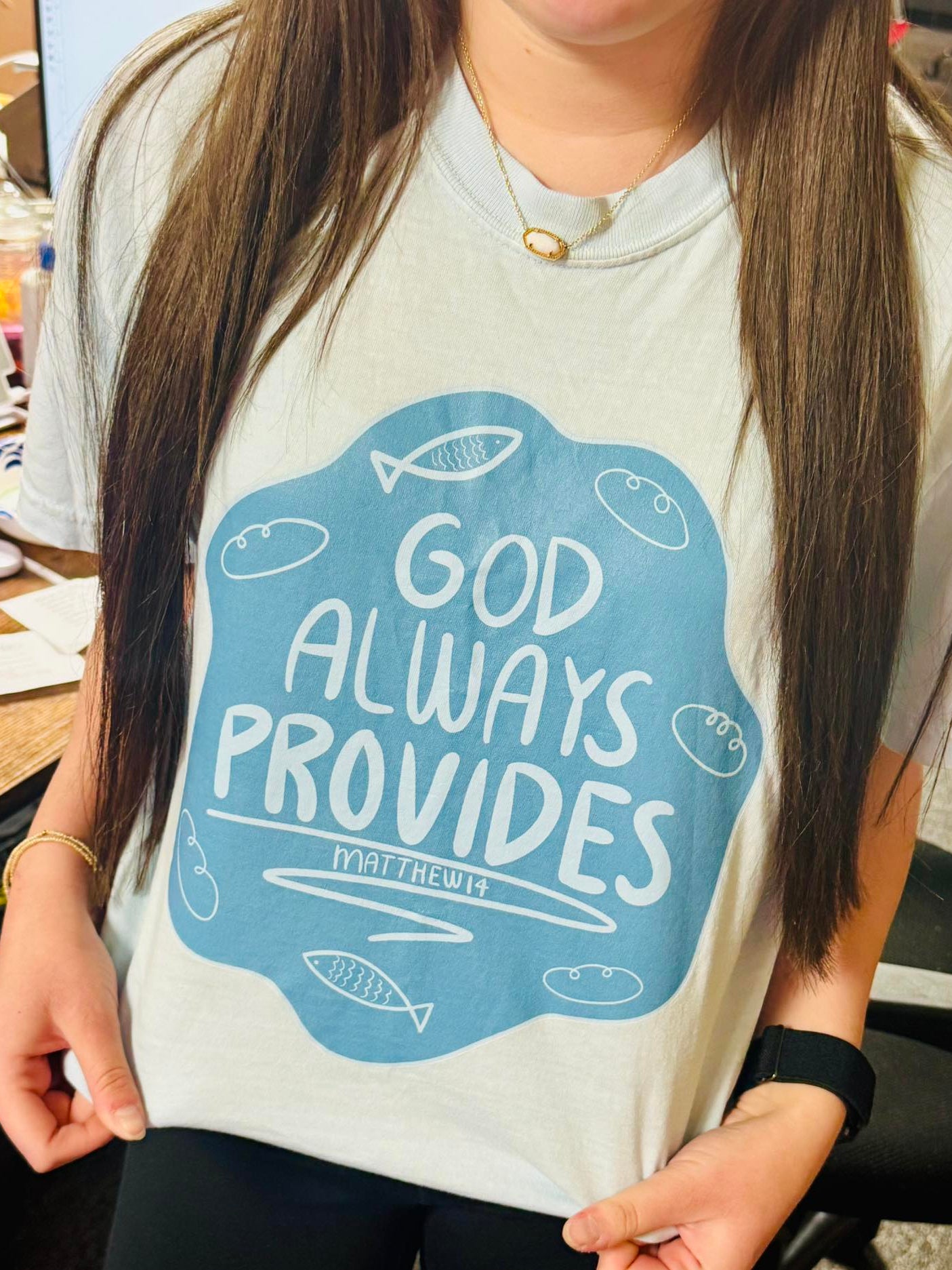 Person wearing a t-shirt with 'God Always Provides' text and fish illustrations.