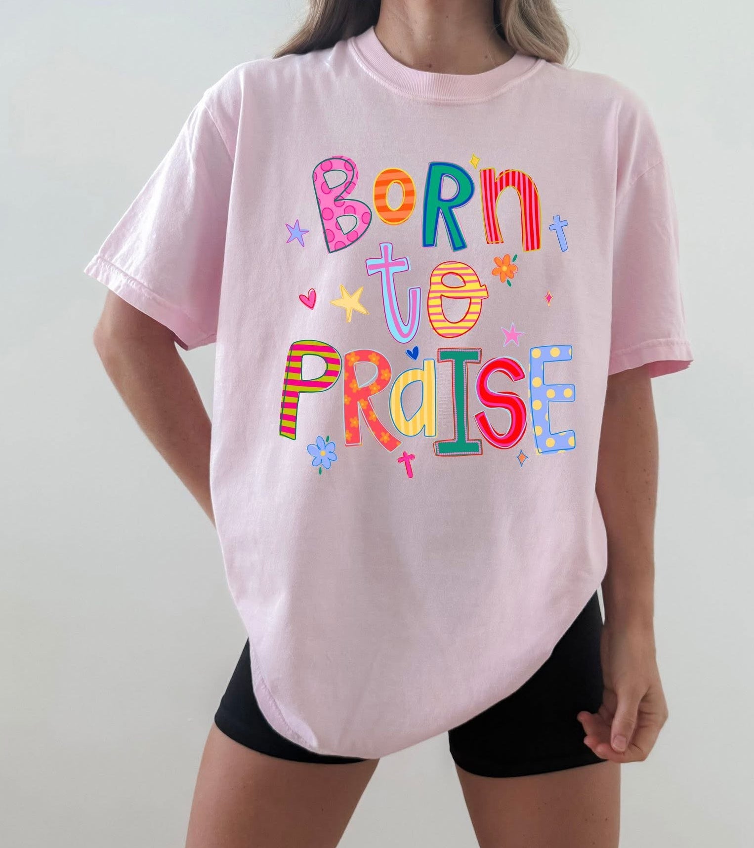 Person wearing a pink t-shirt with colorful text design on a plain background