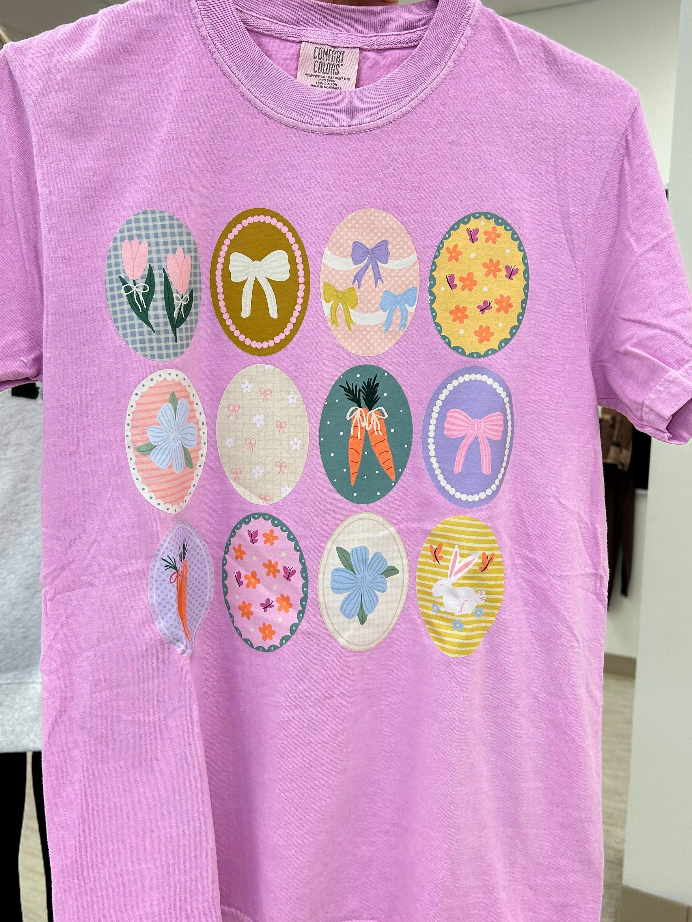 Purple t-shirt with colorful graphic designs on a hanger, held by a person.