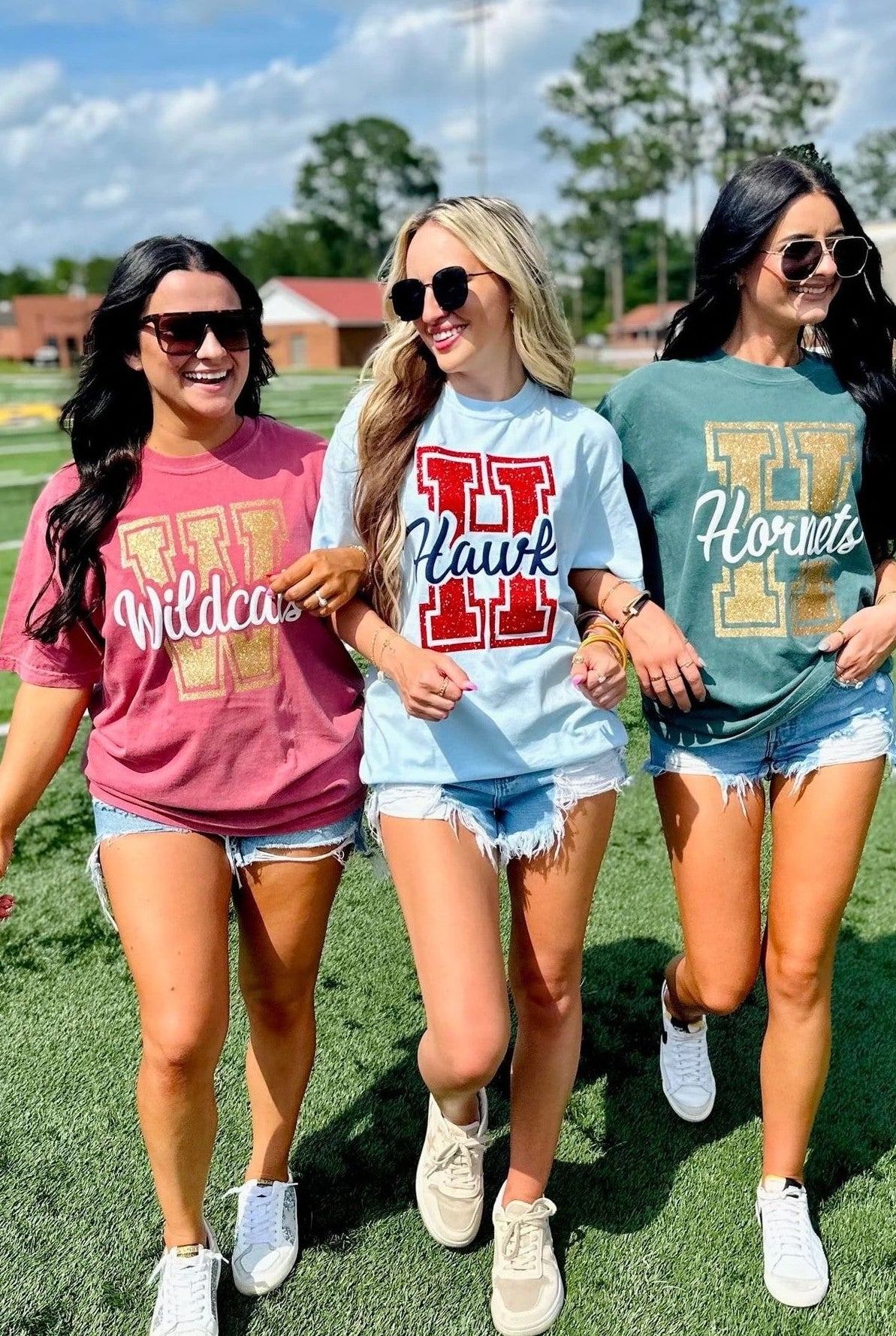 Three women wearing school spirit shirts on a sports field